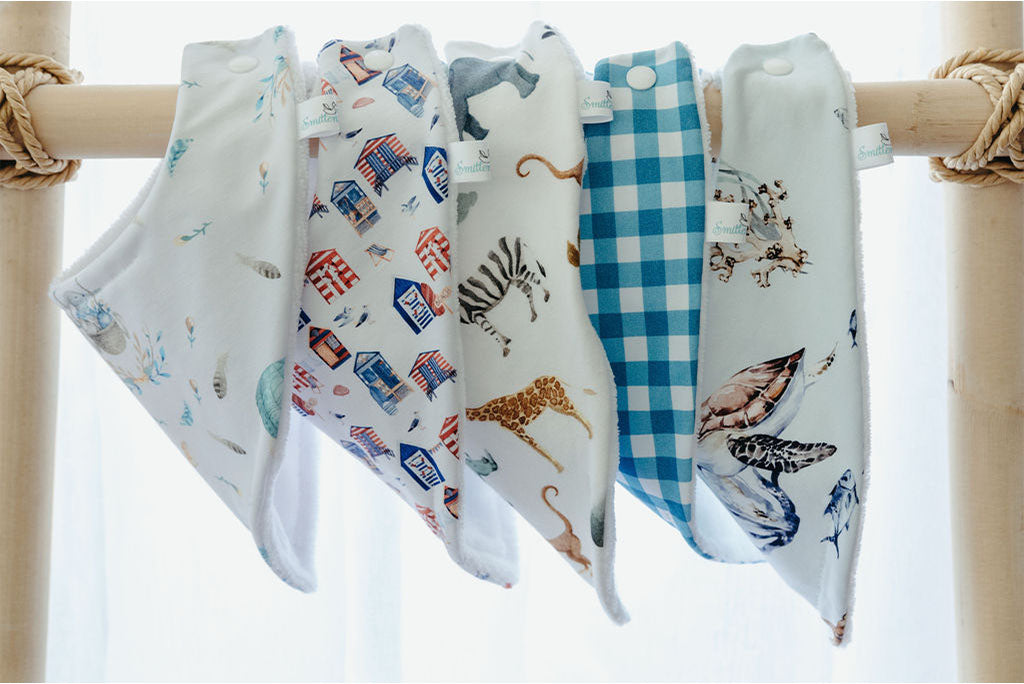 Handmade in Australia Terry cloth bibs with animal, blue gingham, and beach shed prints hanging on a rack.