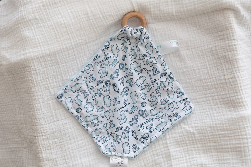 Animals printed in blue on the front of a comforter. Beechwood Teether clipped to comforter