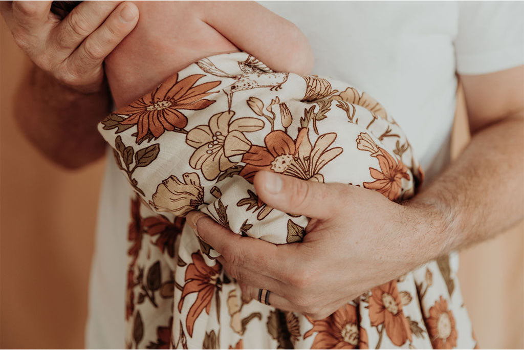 Dad holding baby in floral muslin wrap.