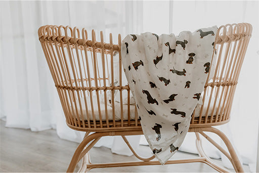 Basket draped with Dachshund Bamboo Cotton Muslin Wrap. White background with Sausage Dog and paw print imagery.