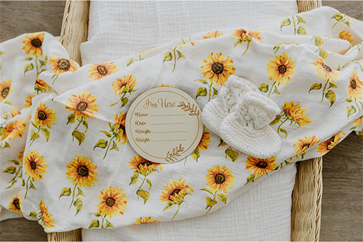 Bamboo Cotton Muslin Wrap Swaddle printed with bright yellow sunflowers. Draped over a Basinet.