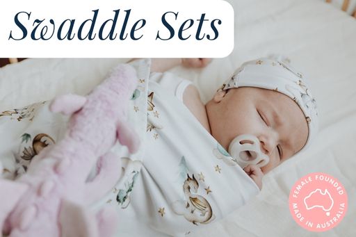 Baby swaddled in a jersey wrap printed with dragons. Dragon Jellycat on top of sleeping baby