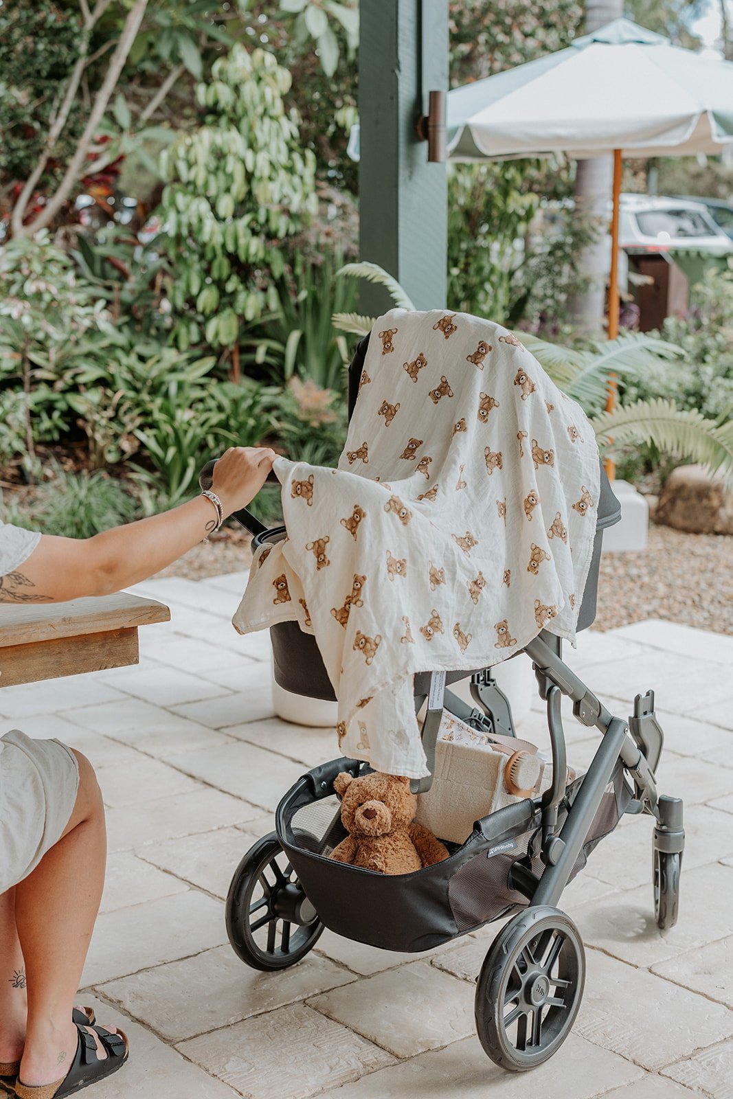 Teddy Bear print Muslin swaddle laying over baby in pram. Jellycat bartholomew bear and nappy caddy in stroller 